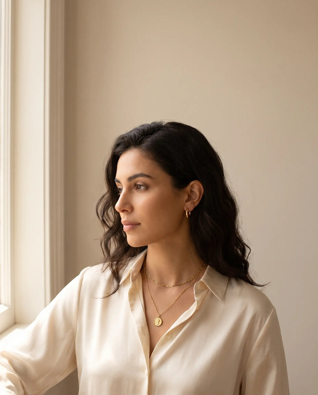 Woman wearing tastefully layered gold jewelry including a short chain necklace, pendant necklace, and hoop earrings