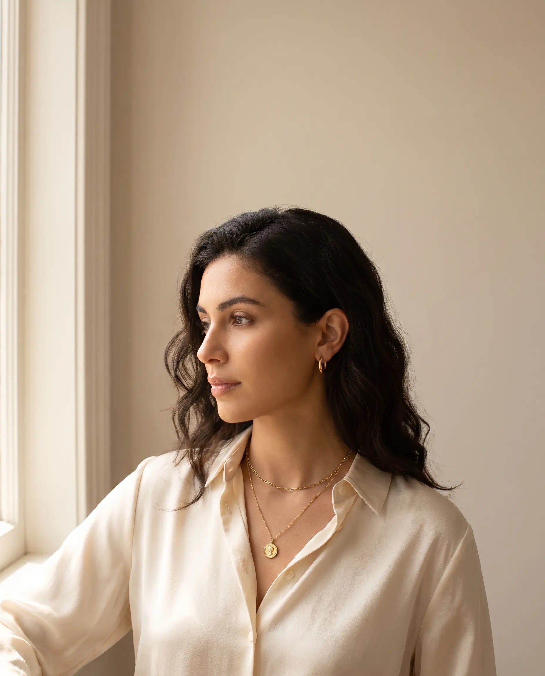 Woman wearing tastefully layered gold jewelry including a short chain necklace, pendant necklace, and hoop earrings