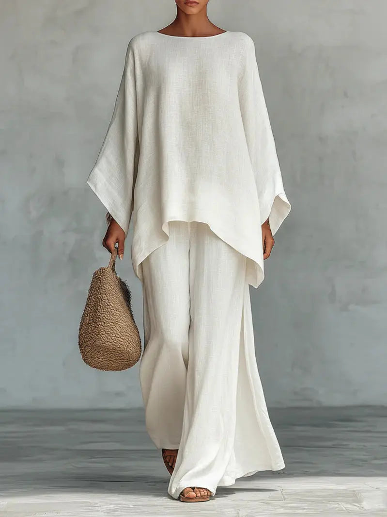 Person wearing a flowing white outfit holding a woven bag against a gray background