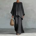 Person wearing a black outfit holding a woven bag against a gray background