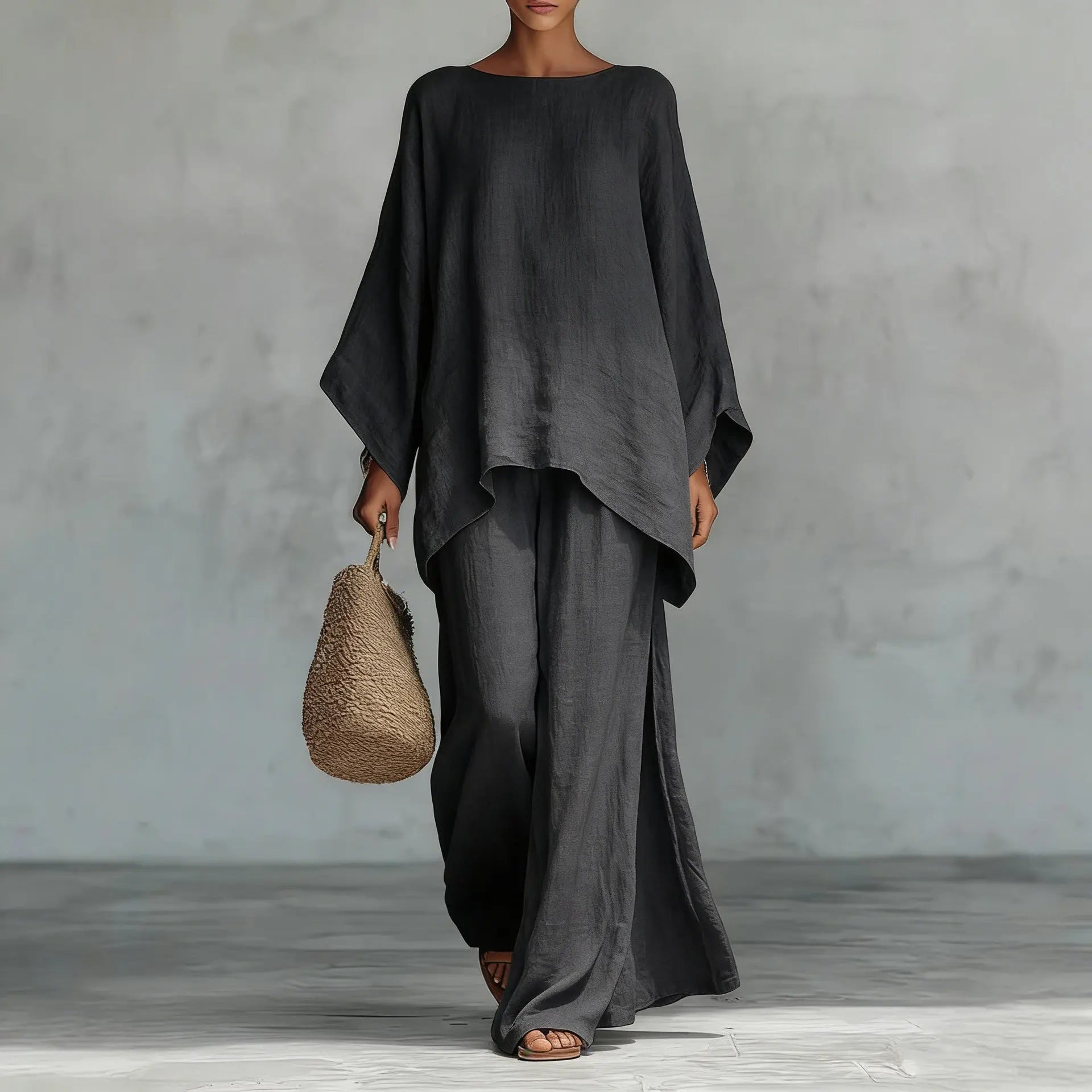 Person wearing a black outfit holding a woven bag against a gray background