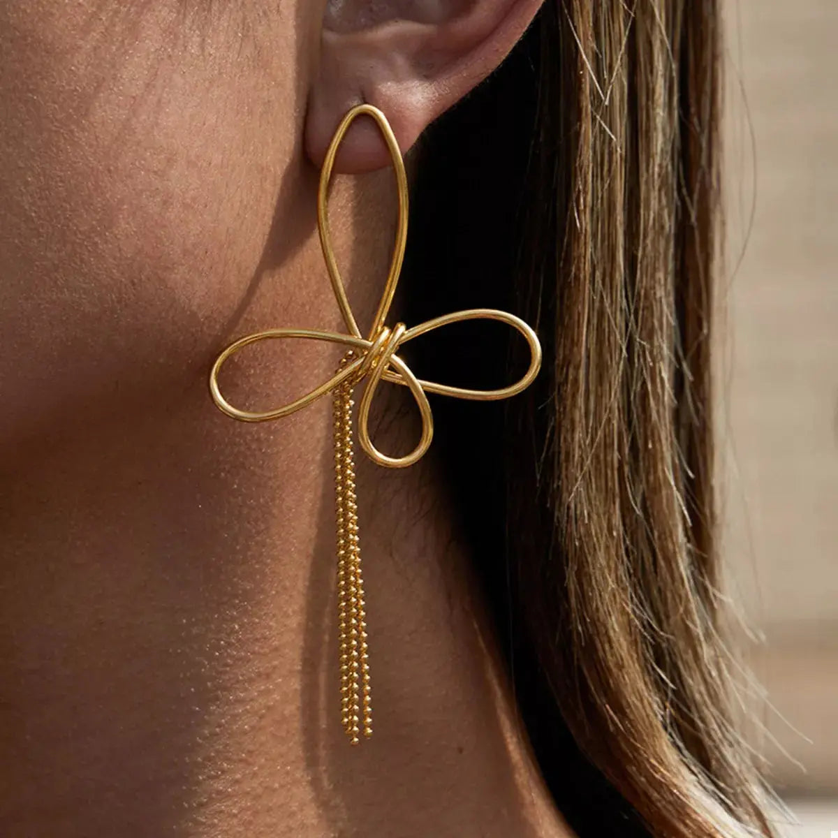 Woman wearing gold tassel bow earrings