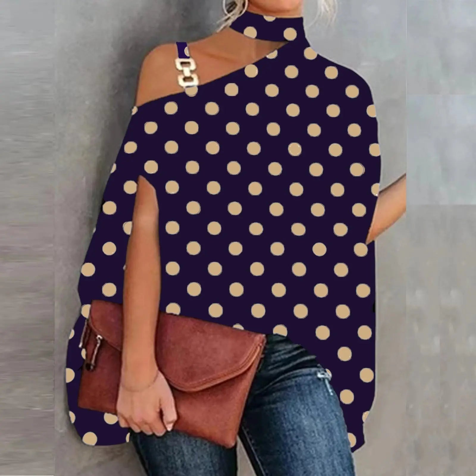 Woman wearing a polka dot top with cut-out shoulders and holding a brown clutch.