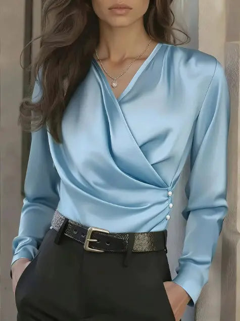 Woman wearing a light blue satin blouse with long sleeves and black pants against a neutral background