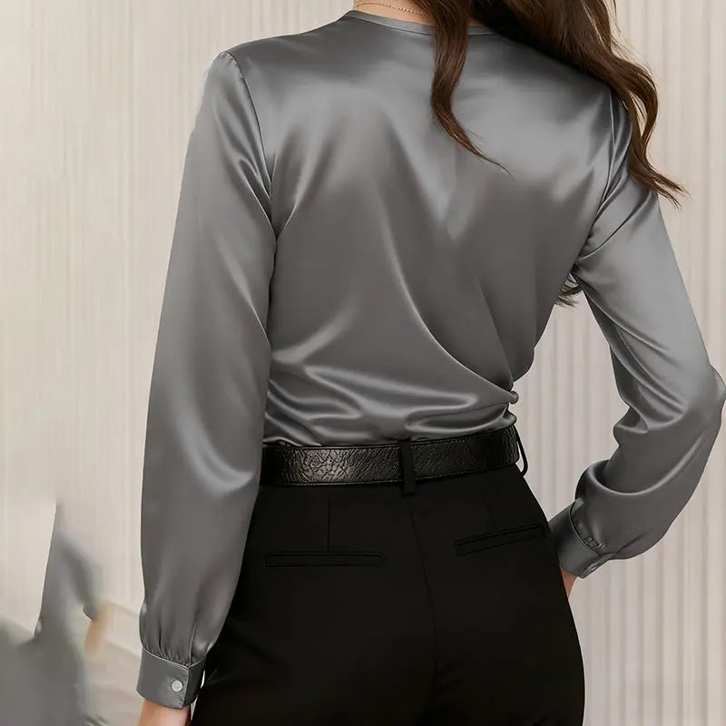 Person wearing a gray satin blouse and black pants against a neutral background