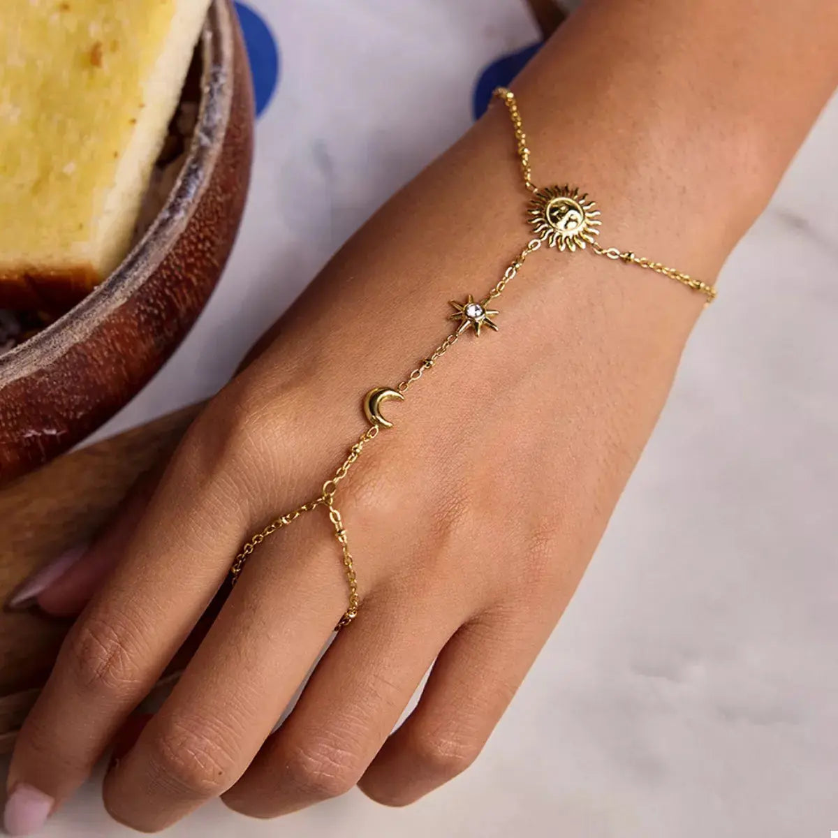 Close-up of sun charm on gold chain bracelet