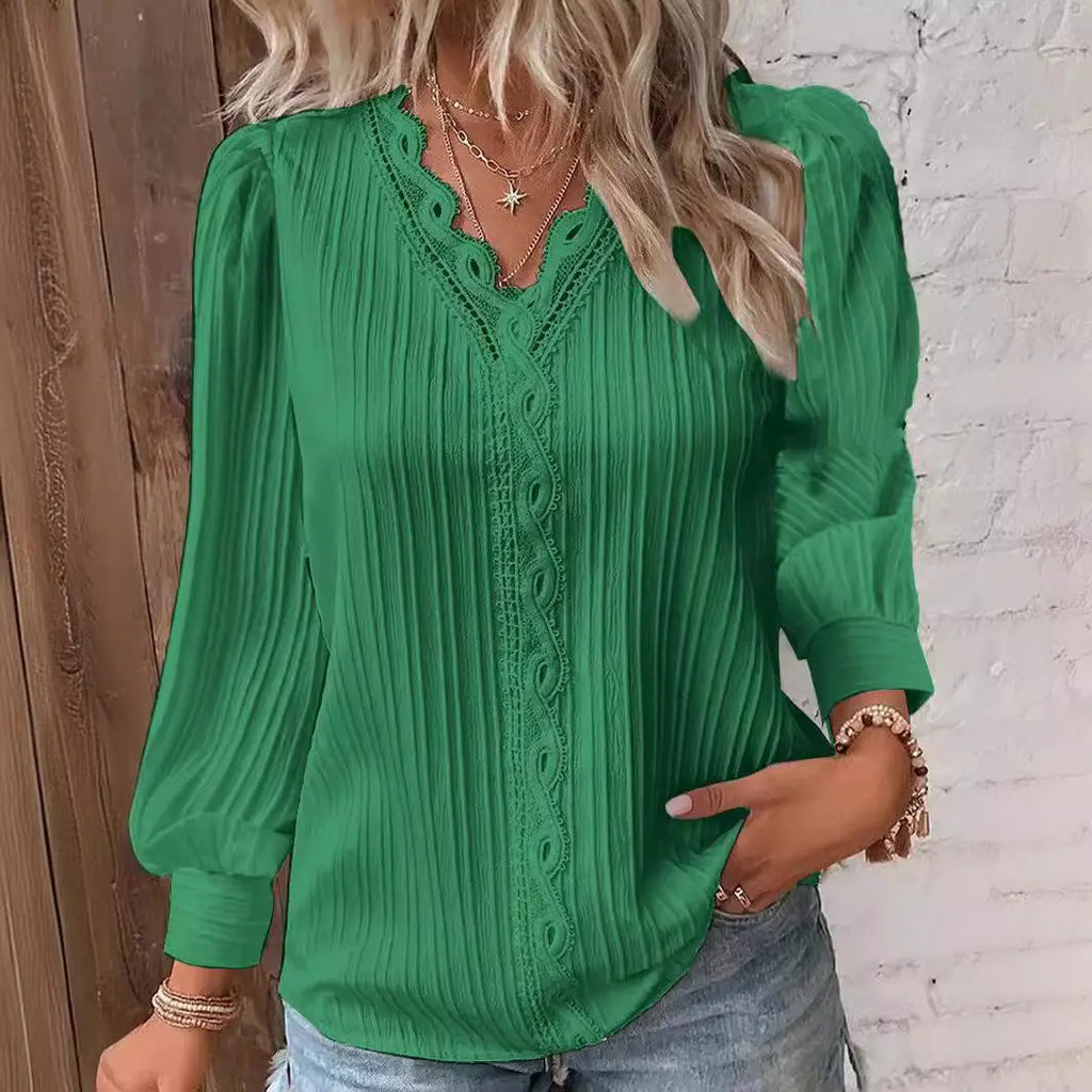Green blouse with intricate detailing worn by a person against a wooden and white brick wall.