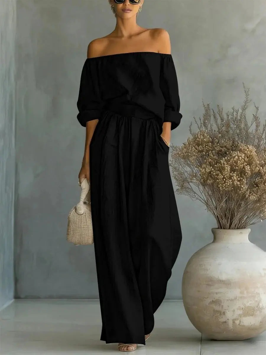 Woman wearing a black off-shoulder dress standing next to a large vase with dried plants.