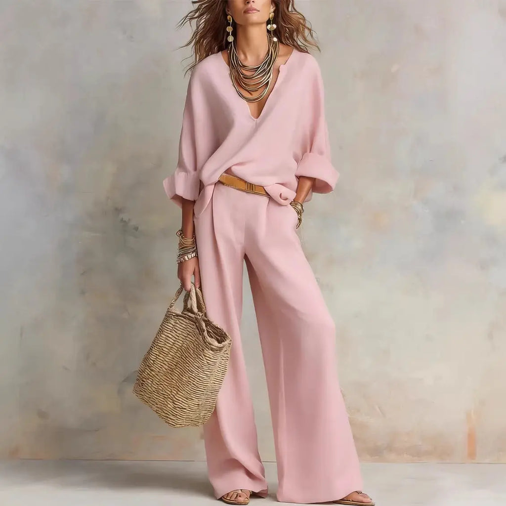 Woman wearing a pink outfit with wide-leg pants and holding a straw bag against a neutral background