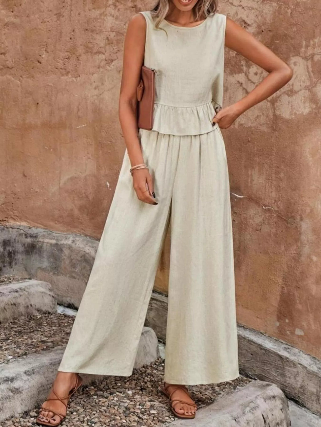 Woman wearing a light-colored jumpsuit standing against a textured wall. Vicsxox.com