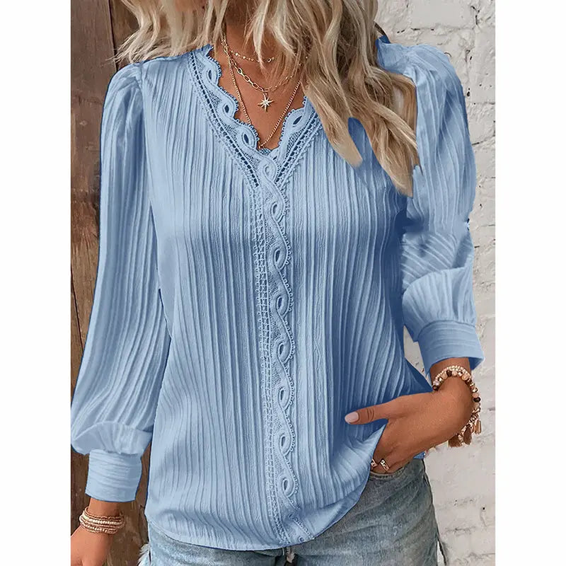 Woman wearing a light blue blouse with lace details and jeans against a neutral background