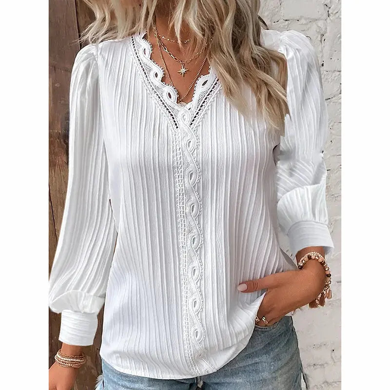 Woman wearing a white blouse with lace details and blue jeans against a light-colored wall.