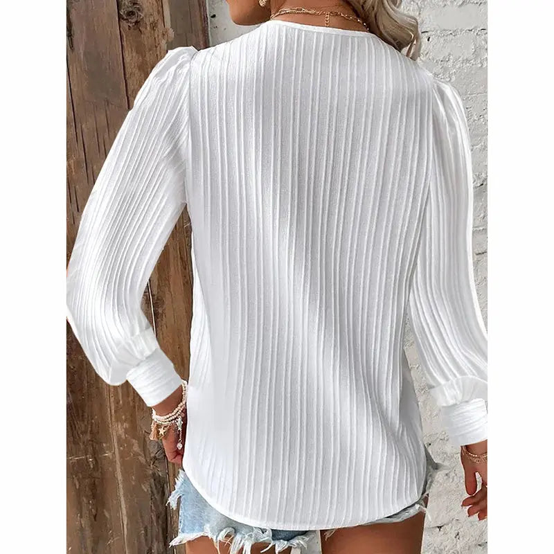 White ribbed blouse worn by a person against a wooden and stone wall.