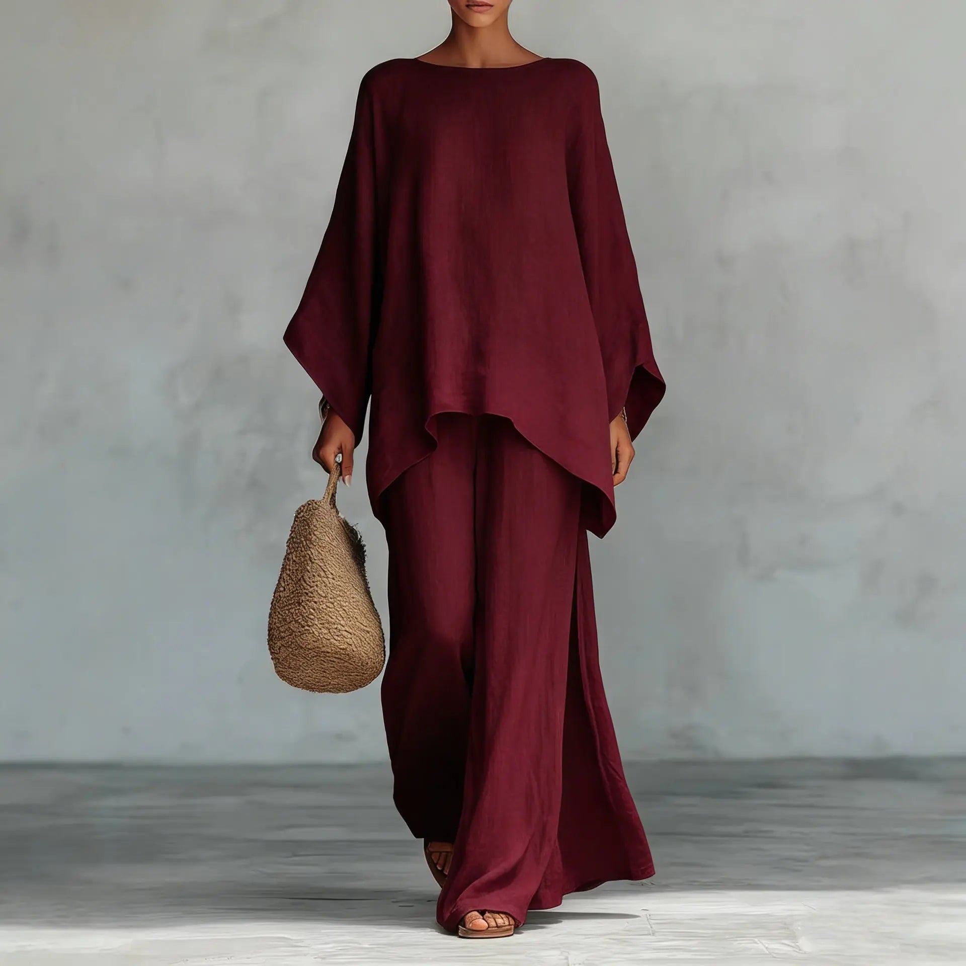 Person wearing a burgundy outfit holding a woven bag against a gray background
