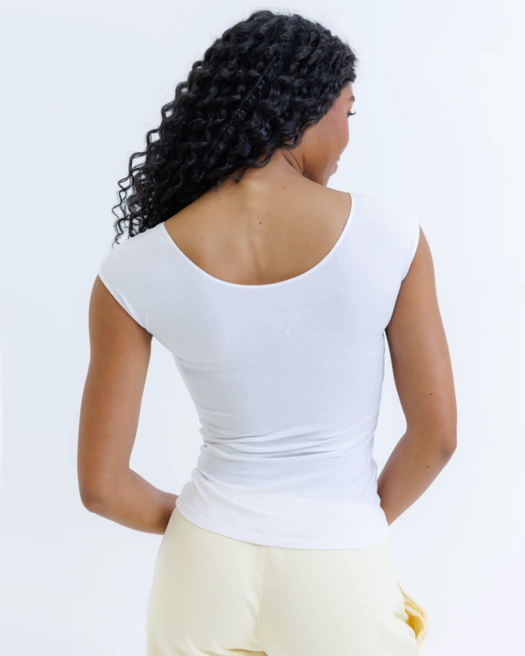 Person wearing a white top and light-colored pants on a plain background