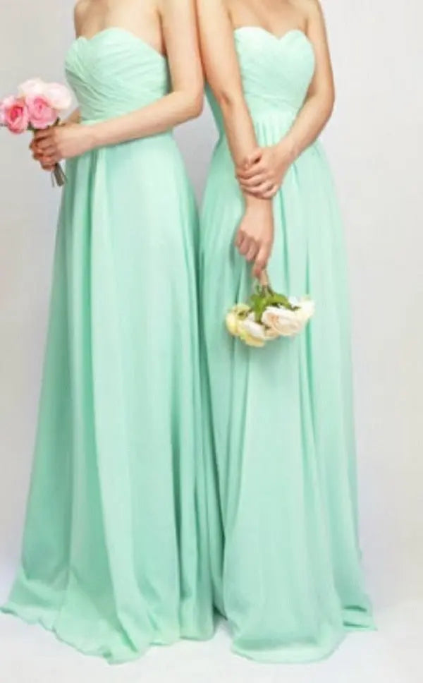 Two women wearing mint green strapless dresses holding flower bouquets on a plain background