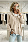 A woman takes a mirror selfie in a clothing boutique wearing a beige lace-up hooded knit sweater, a white t-shirt, and light-wash distressed jeans. Vicsxox.com