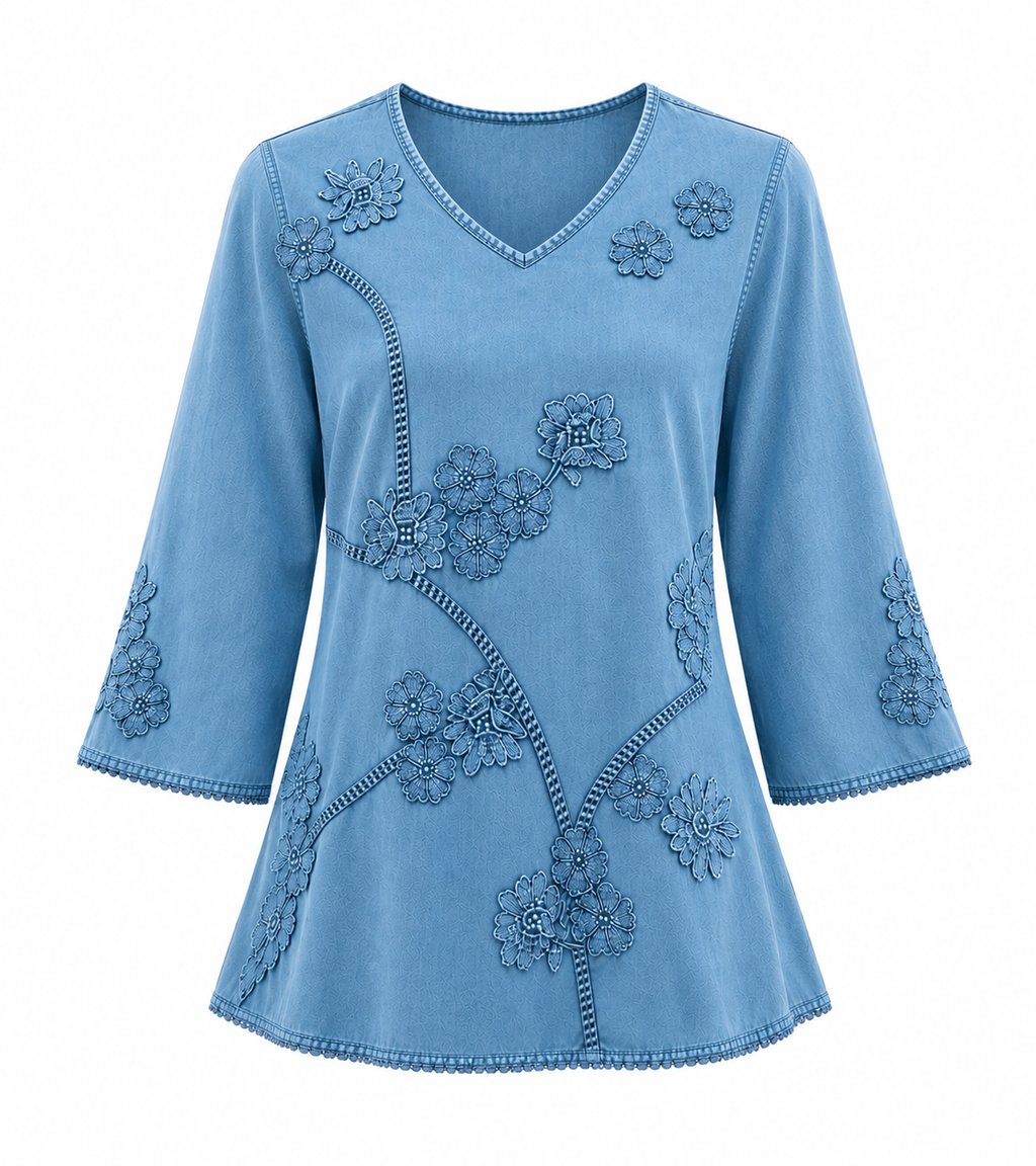 A light blue denim-style top with 3/4 sleeves, a V-neckline, and intricate floral embroidery with contrasting whipstitch detailing, shown against a plain white background. Vicsxox.com