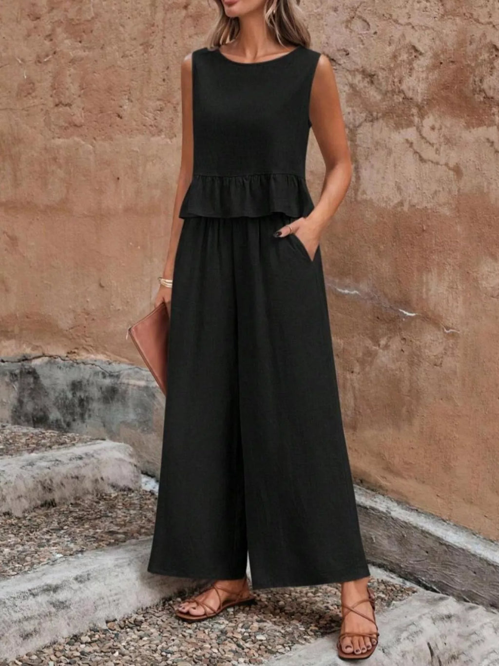 Woman wearing a black jumpsuit standing against a textured wall. Vicsxox.com