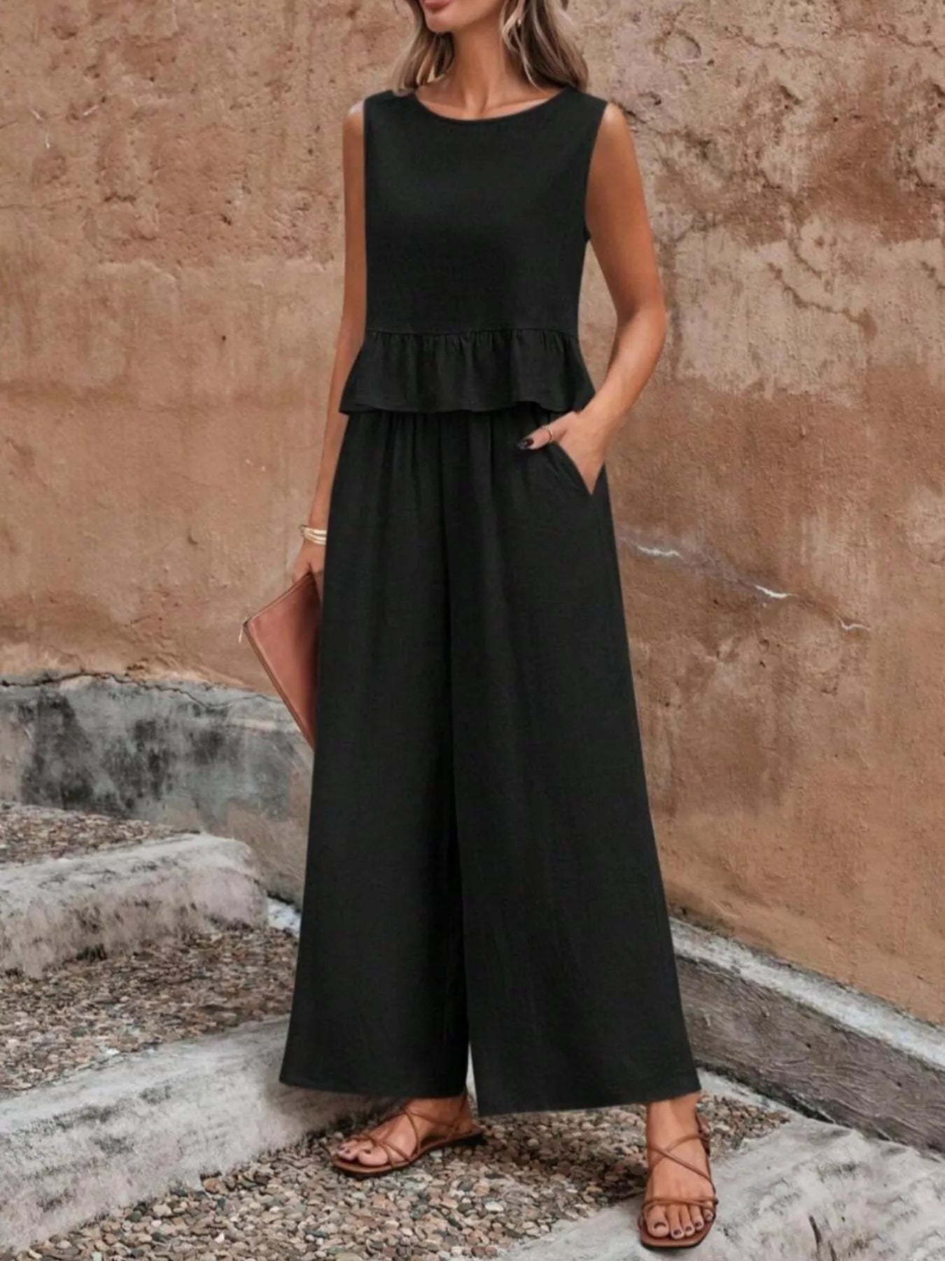 Woman wearing a black jumpsuit standing against a textured wall. Vicsxox.com