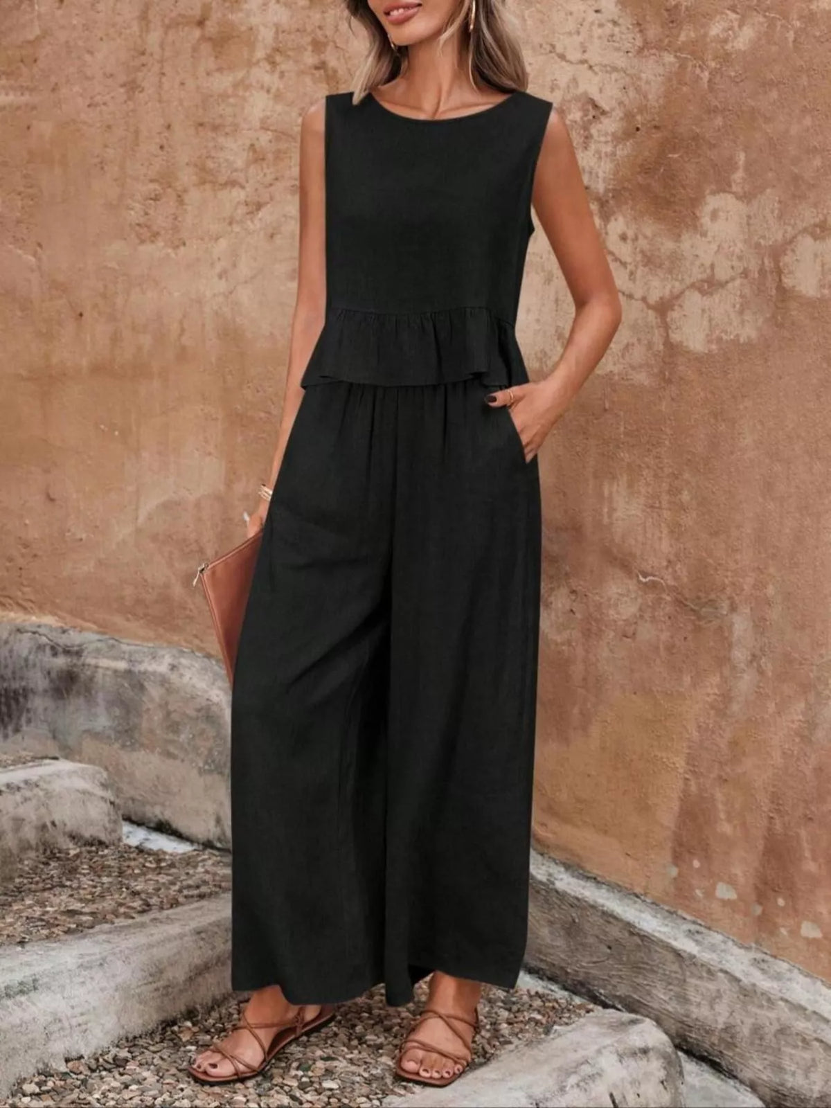 Woman wearing a black sleeveless jumpsuit against a textured wall. Vicsxox.com