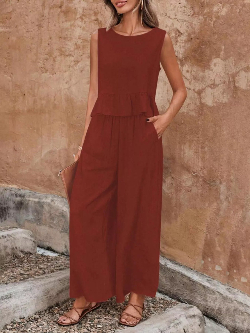 Woman wearing a rust-colored jumpsuit against a textured wall. Vicsxox.com