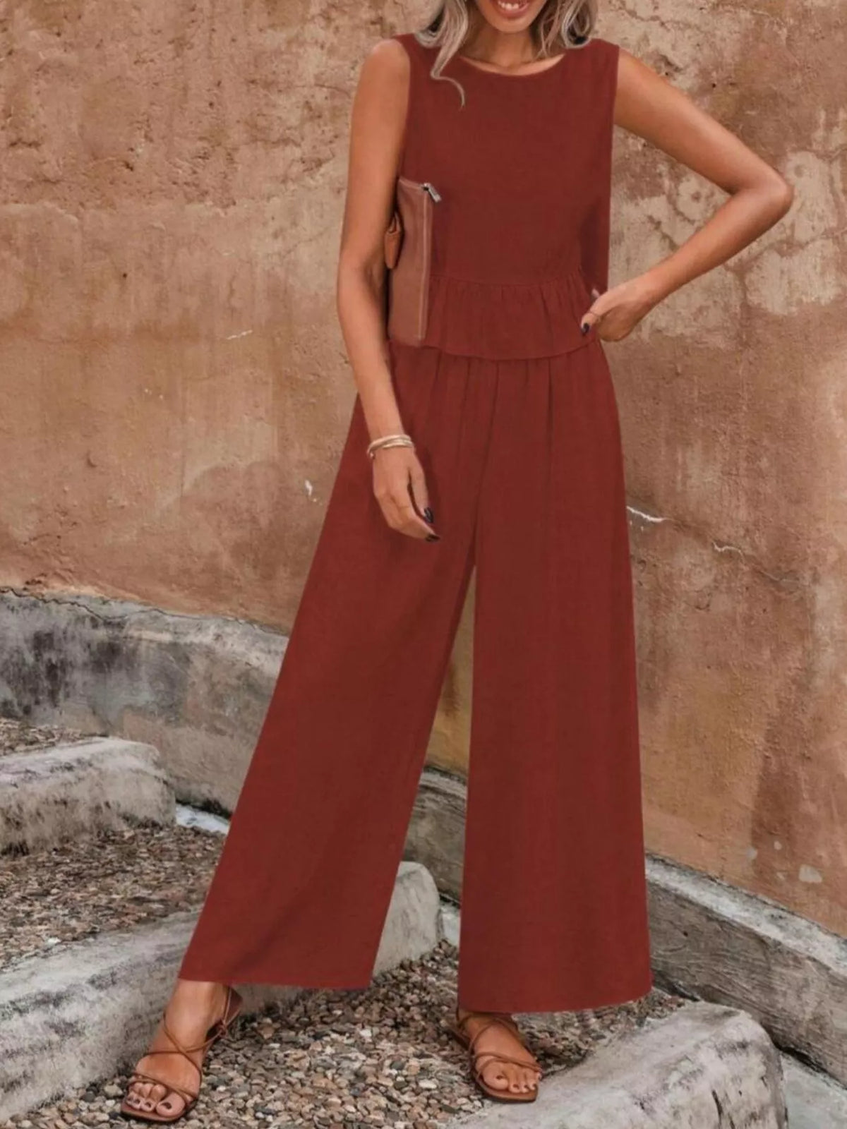 Woman wearing a rust-colored jumpsuit standing against a stone wall. Vicsxox.com