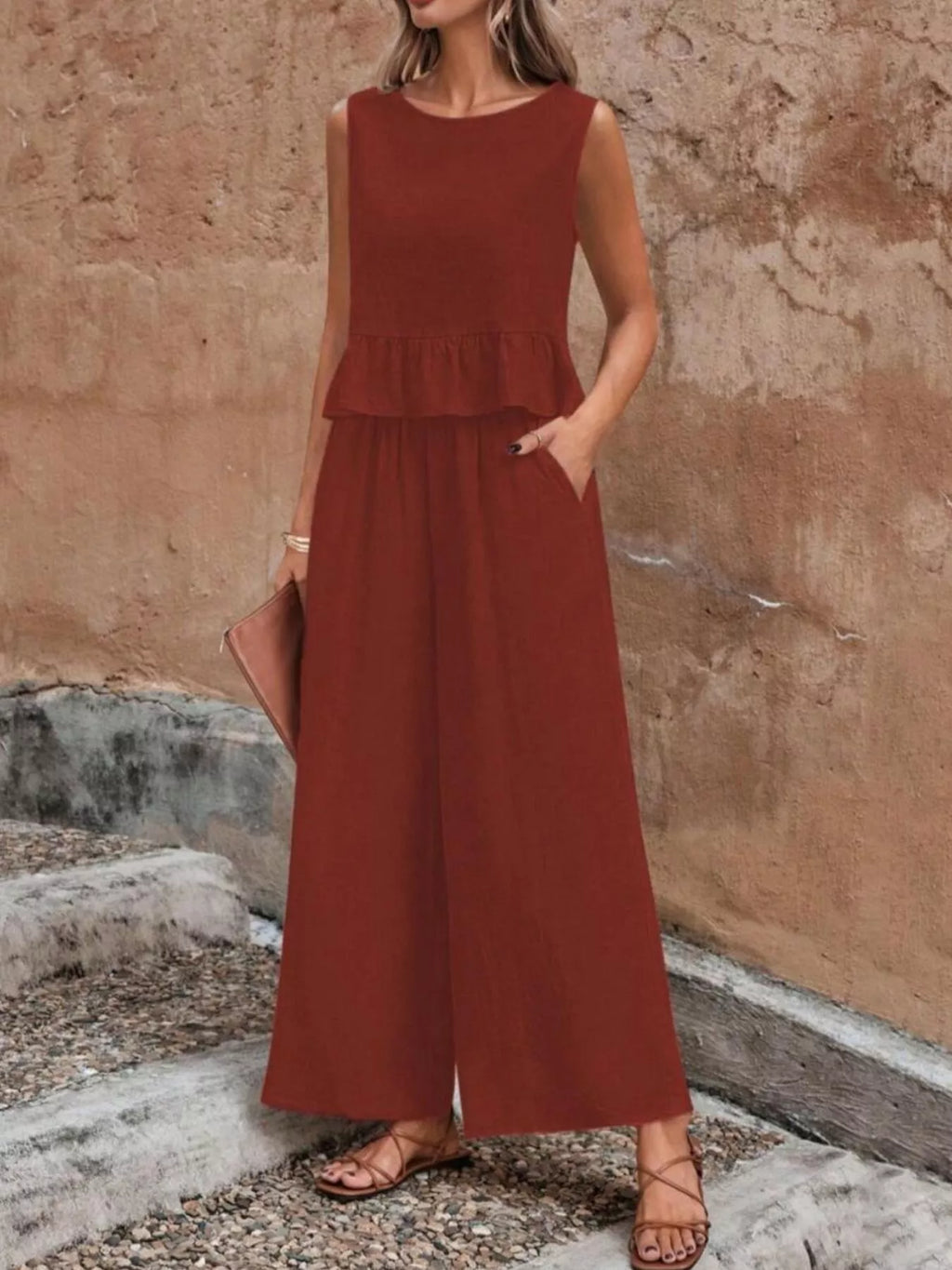 Woman wearing a rust-colored jumpsuit against a stone wall. Vicsxox.com