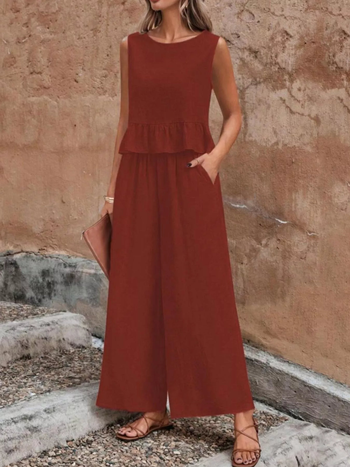 Woman wearing a rust-colored jumpsuit against a stone wall. Vicsxox.com