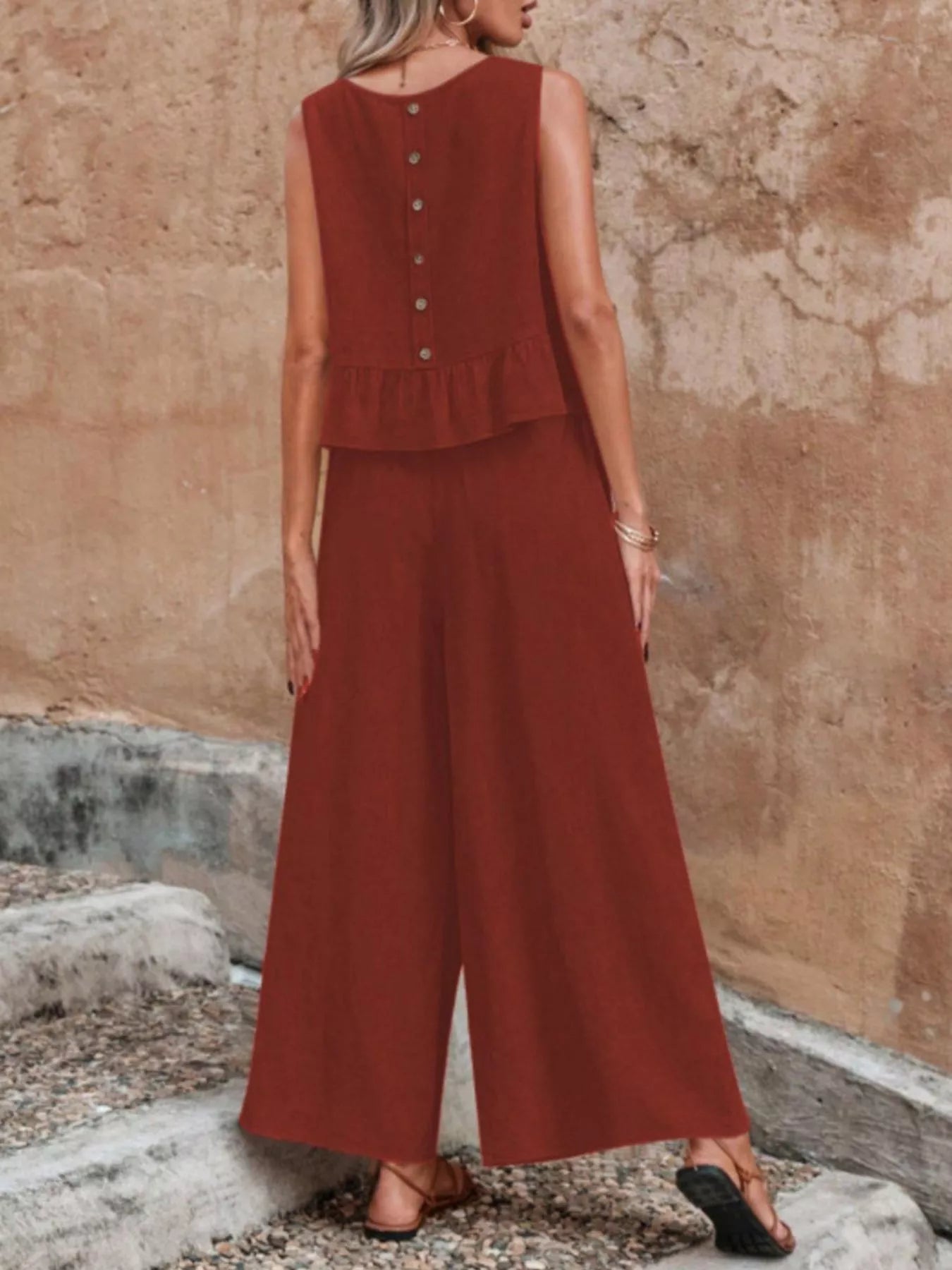 Woman wearing a rust-colored sleeveless top and wide-leg pants against a textured wall. Vicsxox.com