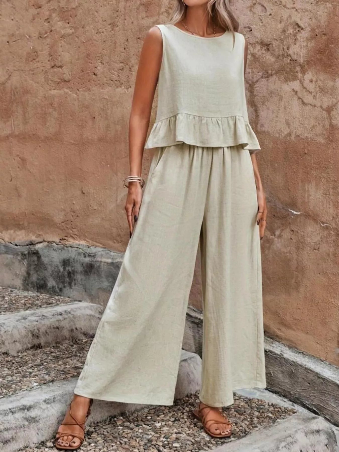 Woman wearing a light green peplum top and wide-leg pants against a textured wall. Vicsxox.com