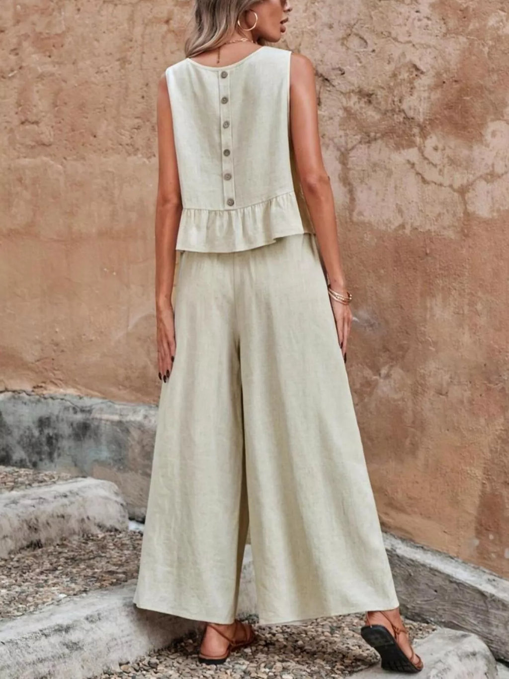 Woman wearing a light green sleeveless top and wide-leg pants against a textured wall. Vicsxox.com