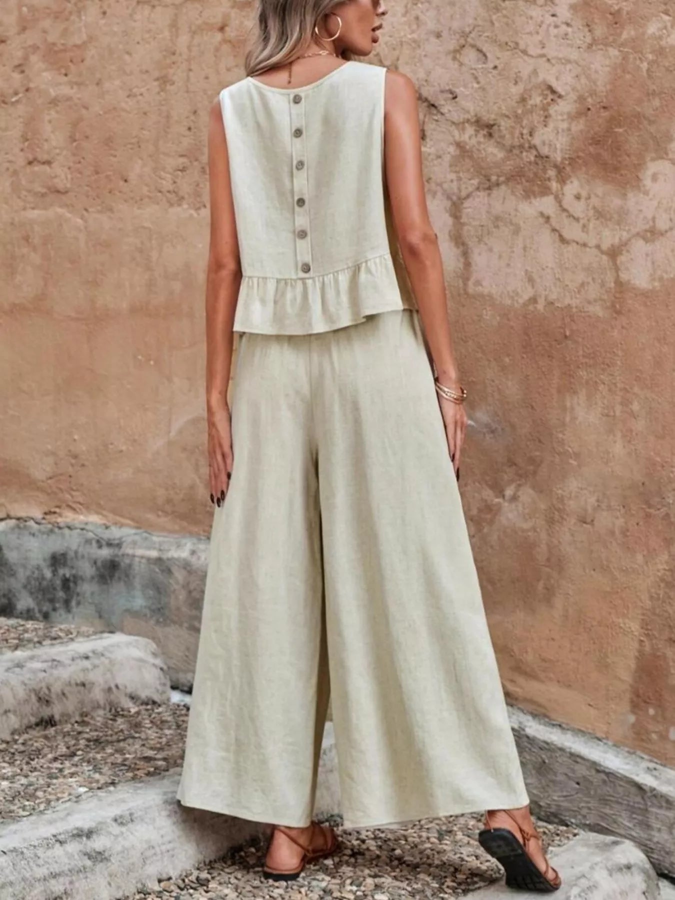 Woman wearing a light green sleeveless top and wide-leg pants against a textured wall. Vicsxox.com