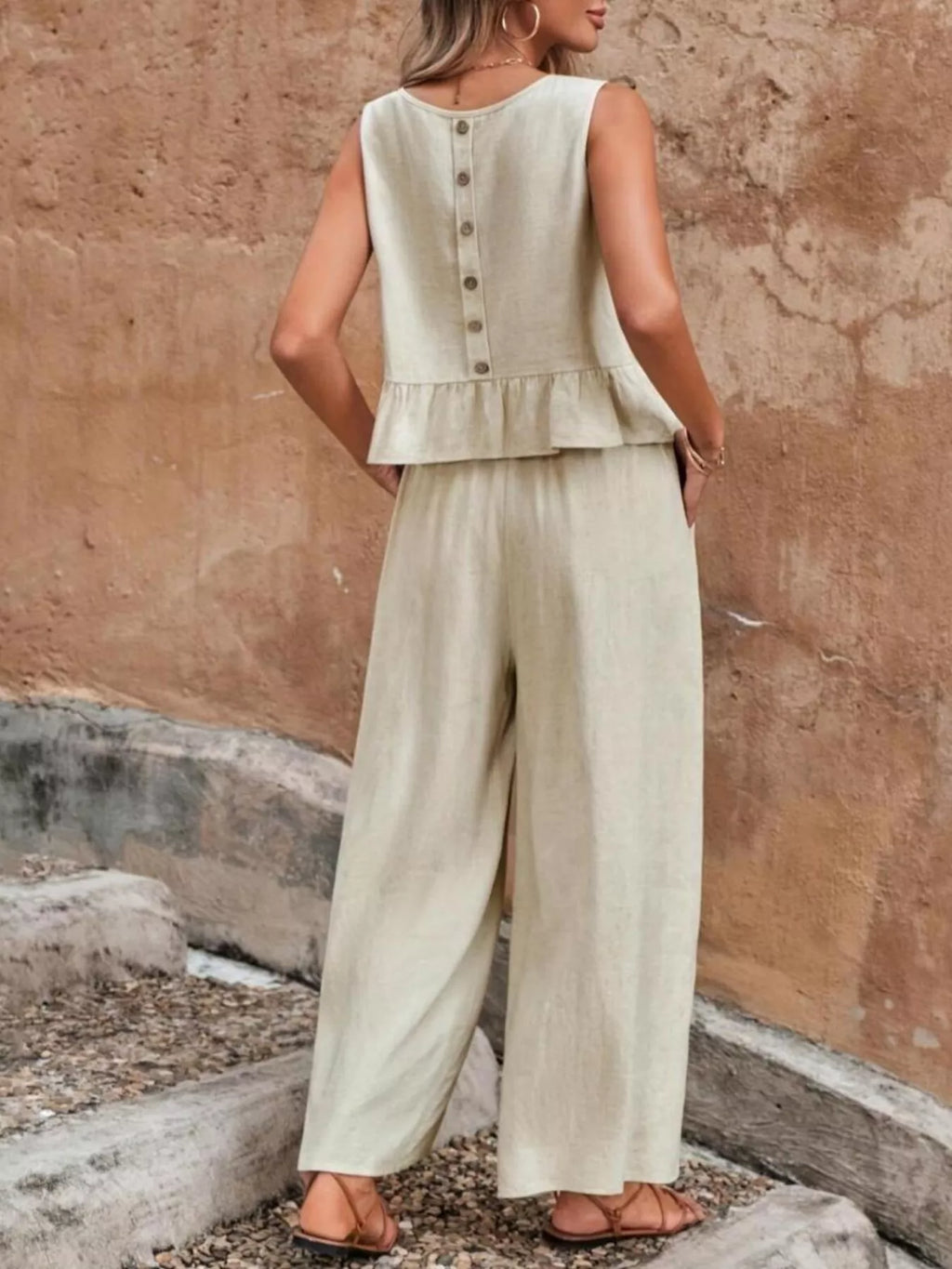 Woman wearing a light green sleeveless top and wide-leg pants against a textured wall. Vicsxox.com