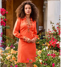 Woman in an orange dress with floral embellishments standing in a garden.