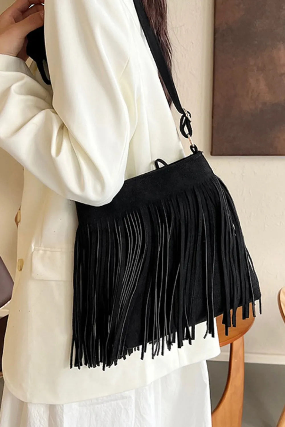 Person wearing a black fringed handbag with a neutral background. Vicsxox.com