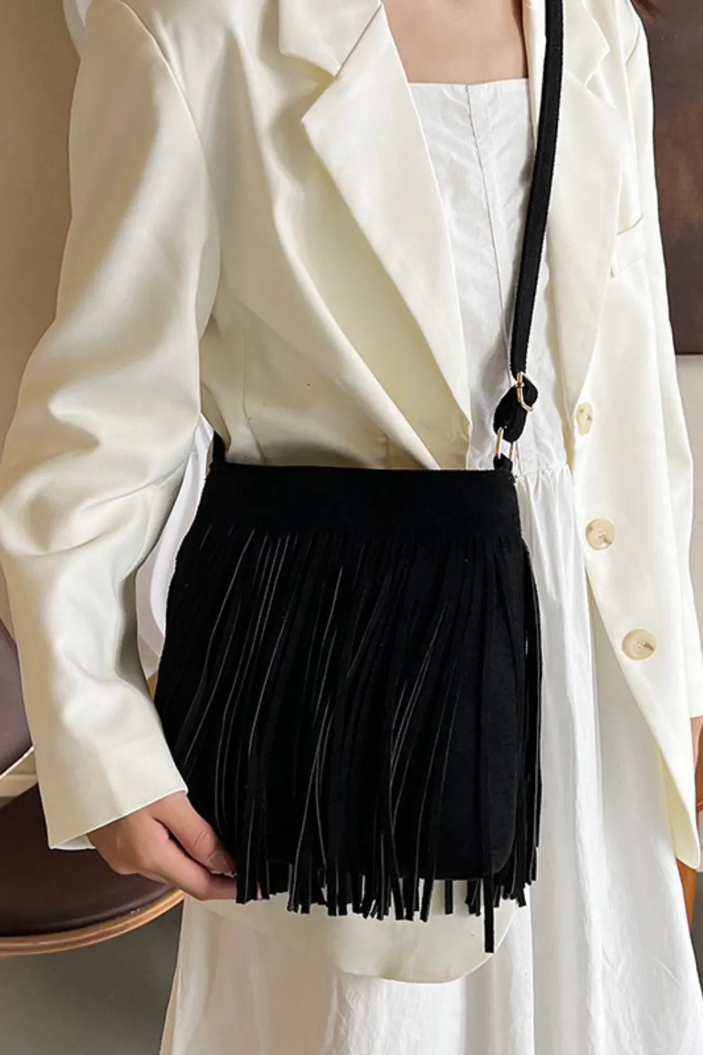 Person wearing a white blazer holding a black fringed handbag. Vicsxox.com