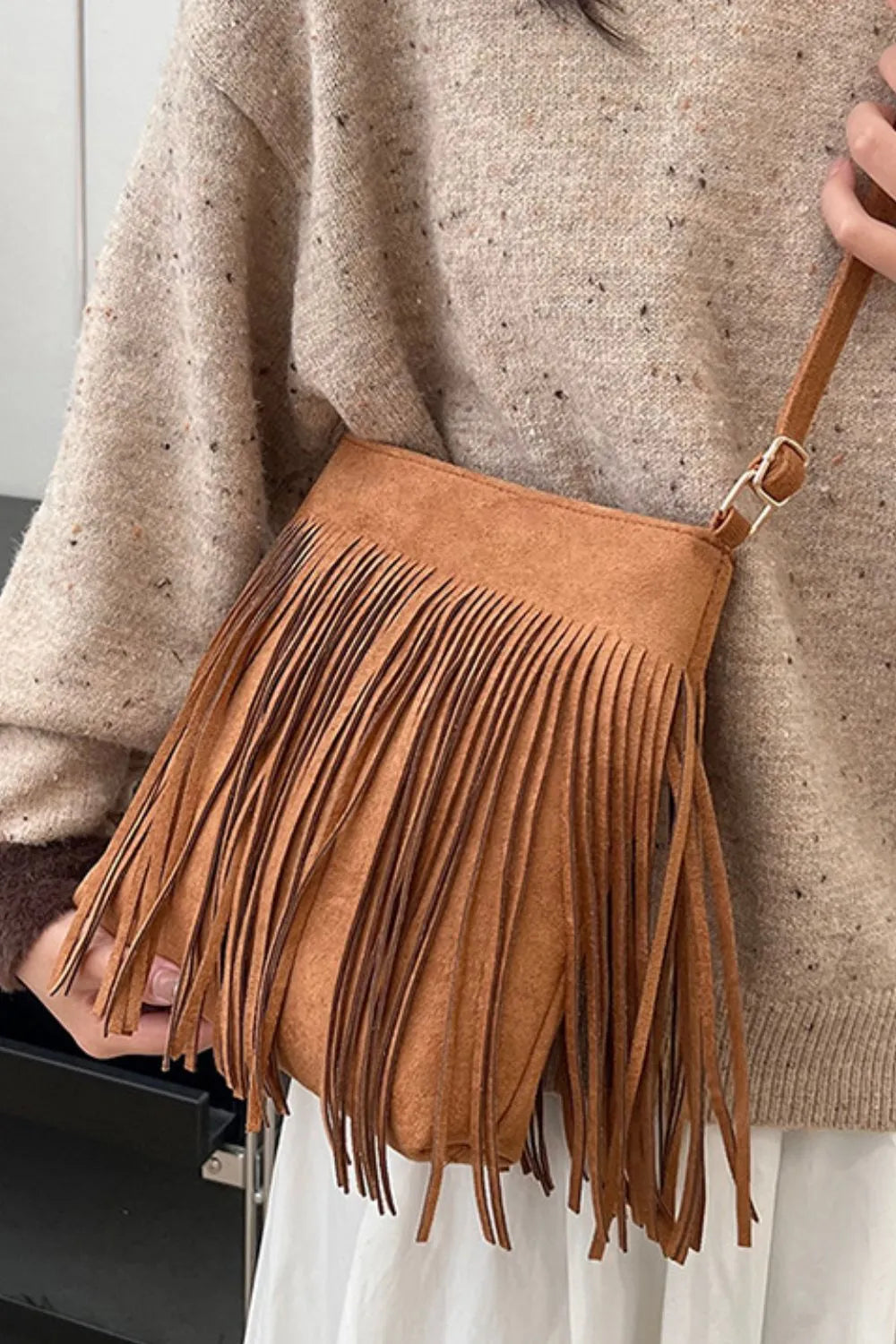 Brown suede handbag with fringe held by a person wearing a beige sweater. Vicsxox.com