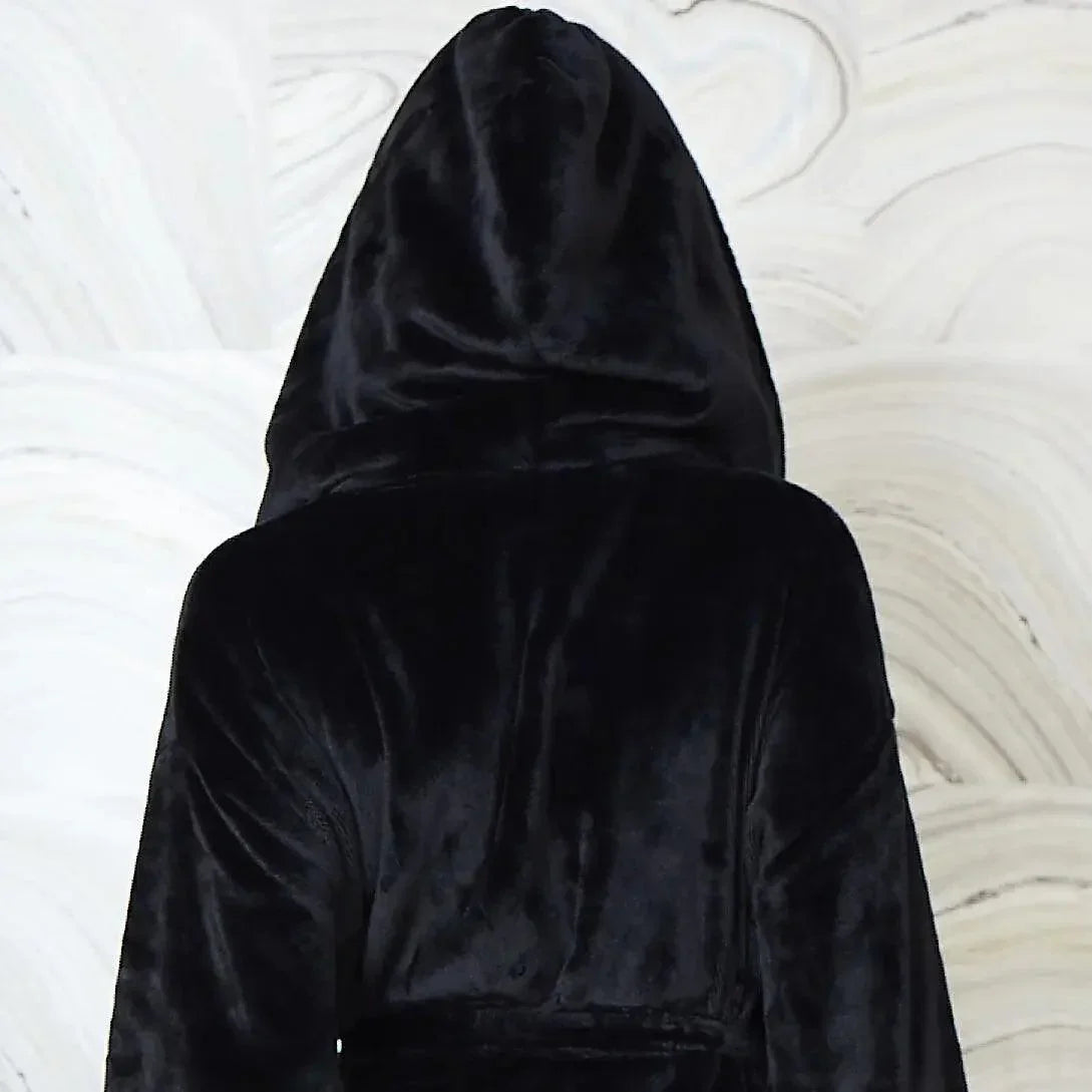 A black hooded robe or cloak made of plush velvet fabric, shown from the back against a white marbled background. Vicsxox.com