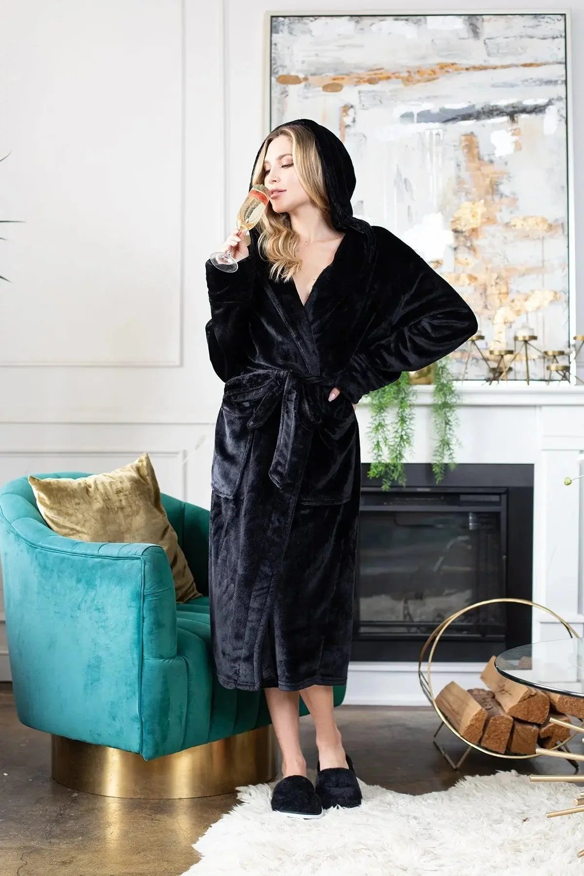 Woman in a black robe standing in a stylish living room with teal chair and fireplace. Vicsxox.com