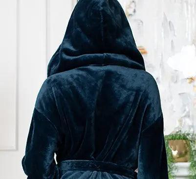 Person wearing a dark blue robe with a hood in a room with white walls and decorative elements. Vicsxox.com