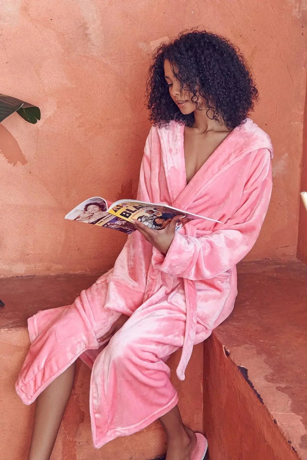 Woman in a pink robe reading a magazine against an orange wall. Vicsxox.com