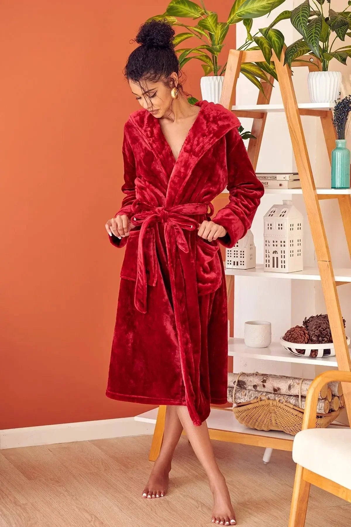 Woman in a red robe standing in a room with an orange wall and a shelf with decor items. Vicsxox.com