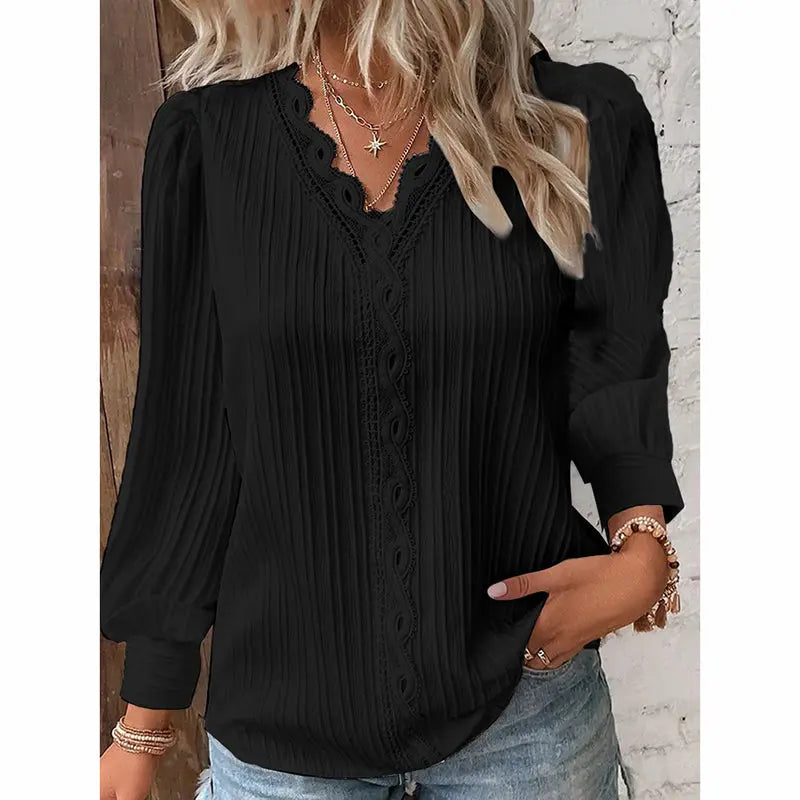Black blouse with long sleeves and buttons worn by a person against a white brick wall.