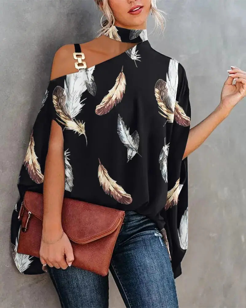 Woman wearing a black off-shoulder top with feather pattern, holding a brown leather clutch against a gray background.