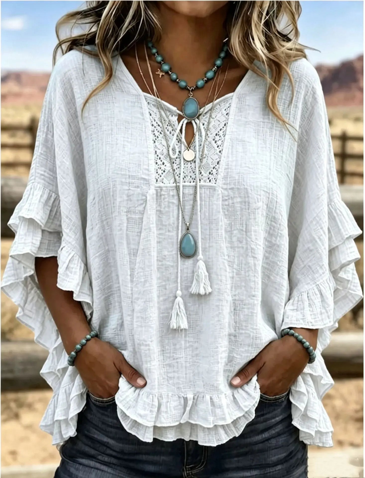 White ruffled blouse with lace details and tassel necklace against a blurred outdoor background