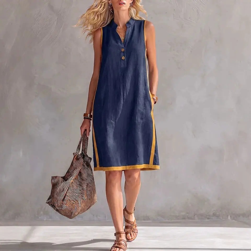 Woman wearing a navy sleeveless dress with gold trim, holding a textured bag against a neutral background.