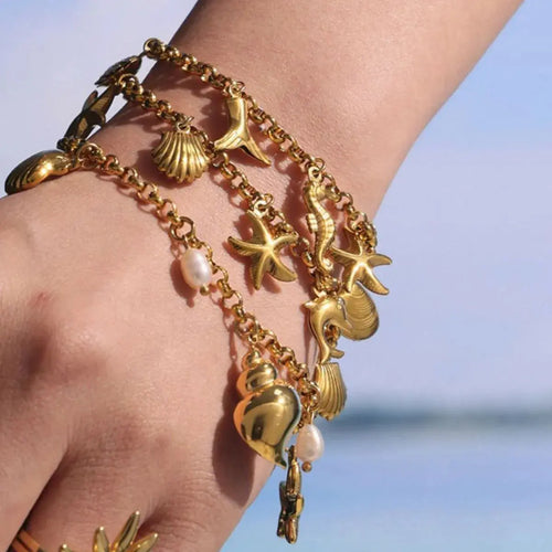 Close-up of sea shell charm on gold bracelet