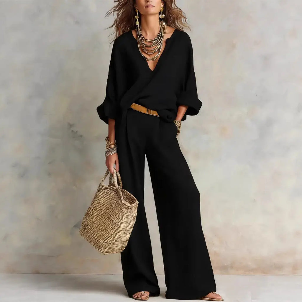 Woman wearing a black outfit with wide-leg pants, holding a woven bag against a neutral background