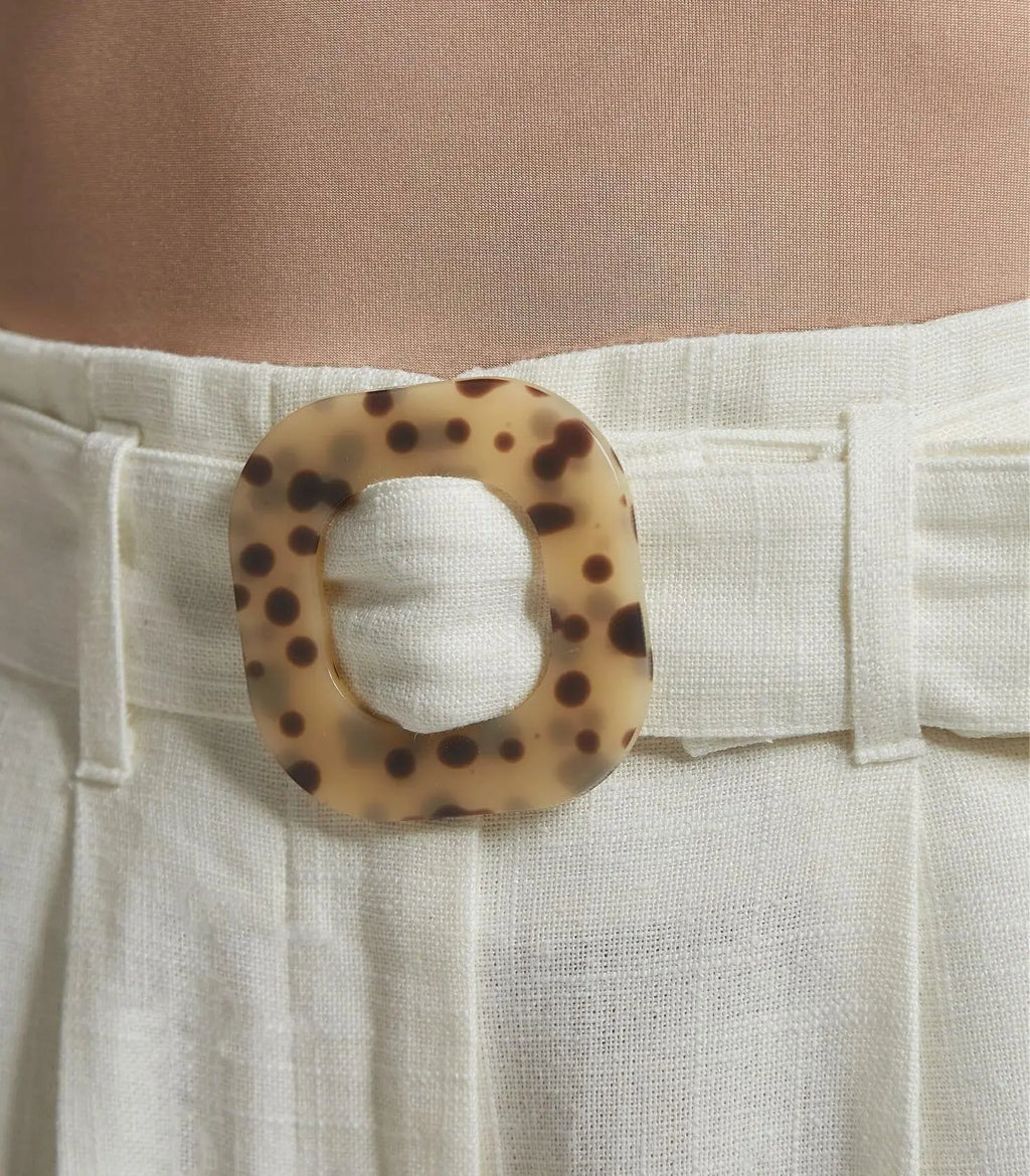 White pants with a leopard print belt buckle worn by a person.